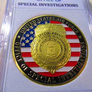 Może przedstawiać: Złoty medalion z czarnym obramowaniem i napisem "United States Air Force Office of Special Investigations" wok&oacute;ł krawędzi. W centrum medalionu znajduje się złota odznaka z napisem "Special Agent" i "Office of Special Investigations Department of the Air Force" wok&oacute;ł krawędzi. Odznaka zawiera r&oacute;wnież stylizowanego orła i napis "The Inspector General 1948".