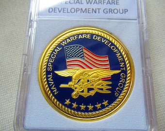 May include: A gold coin with a blue and gold design. The coin features the words "NAVAL SPECIAL WARFARE DEVELOPMENT GROUP" and a depiction of a seal with an American flag.