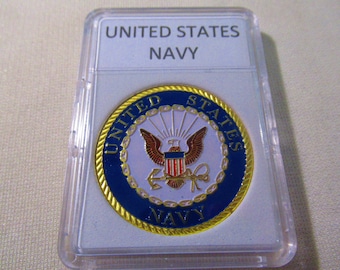 May include: A gold-colored coin with a blue and white seal featuring the United States Navy emblem. The coin is in a clear plastic case with a white label that reads "UNITED STATES NAVY".