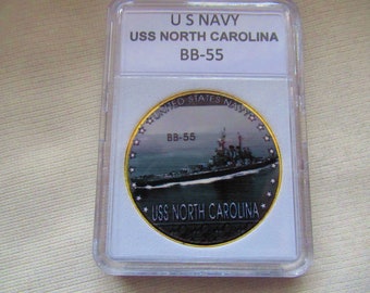 Puede incluir: Una moneda de color dorado con una imagen en blanco y negro del acorazado USS North Carolina. La moneda tiene el texto "United States Navy" y "BB-55" en ella.