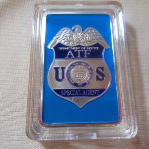 May include: A silver and blue badge with the words "Department of Justice ATF U.S. Special Agent" on it.