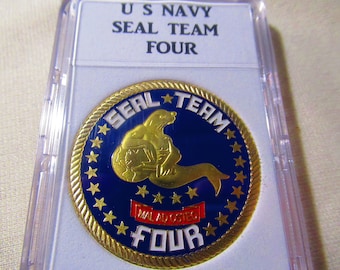 May include: A gold-colored coin with a blue and white design. The coin features a seal holding a globe and the text "SEAL TEAM FOUR" around the edge. The coin is in a plastic case.