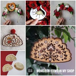 May include: A collection of handmade items including two floral headbands with pretzel and dumpling accents, a white cat sticker holding a dumpling, and several wooden ornaments featuring pyrography designs of roosters and floral patterns.