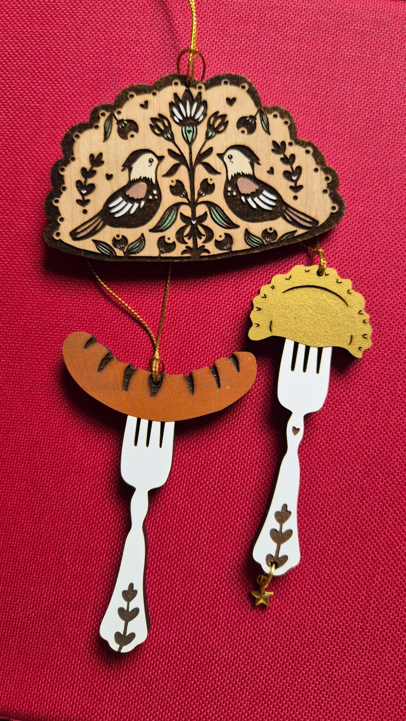 May include: A set of three wooden hanging ornaments featuring a semi-circular plaque with two birds and floral motifs, a brown sausage on a white fork, and a gold-colored dumpling on a white fork with a small star charm attached to the handle.