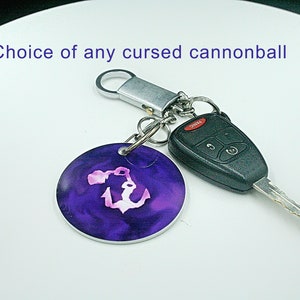 May include: A purple and pink anchor keychain with a silver key ring and a black car key. The keychain says "Choice of any cursed cannonball".