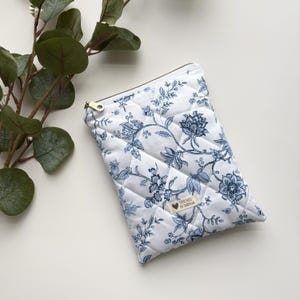 Może przedstawiać: Biała pikowana kosmetyczka z zamkiem błyskawicznym, z niebieskim wzorem kwiatowym i napisem "Stitched by Tashiana".