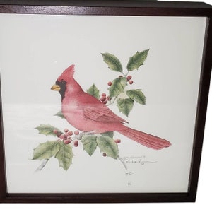 May include: A framed print of a red cardinal perched on a holly branch with red berries. The print is signed "Tom Hanson" and "D. Dahlke".