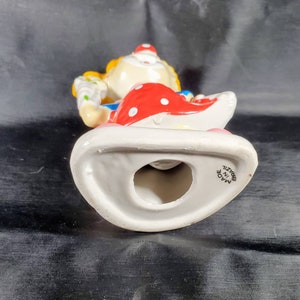 Pu&ograve; includere: Statuetta di clown in ceramica con cappello rosso a pois bianchi e base bianca. Il clown ha i capelli gialli, un abito blu e rosso e tiene in mano un oggetto colorato. La statuetta &egrave; contrassegnata "Made in Brazil".