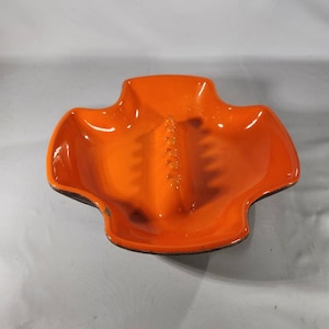 May include: Orange ceramic ashtray with four points and a center divider.