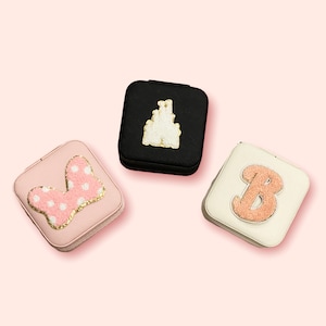 May include: Three small square compact mirrors with different designs. One has a pink bow with white polka dots, one has a white castle, and one has a gold letter B.
