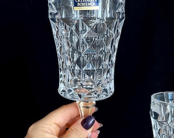May include: Clear crystal goblet with a diamond-cut pattern. The goblet is held up against a black background. The label reads "Crystalite Bohemia Czech Republic".