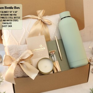 May include: A gift box containing a 50" x 60" white knit blanket, a 17 oz stainless steel bottle, a notebook, a pen, a candle, matchsticks, chocolate, and fuzzy socks. The box includes text listing these items and the title Green Bottle Box.