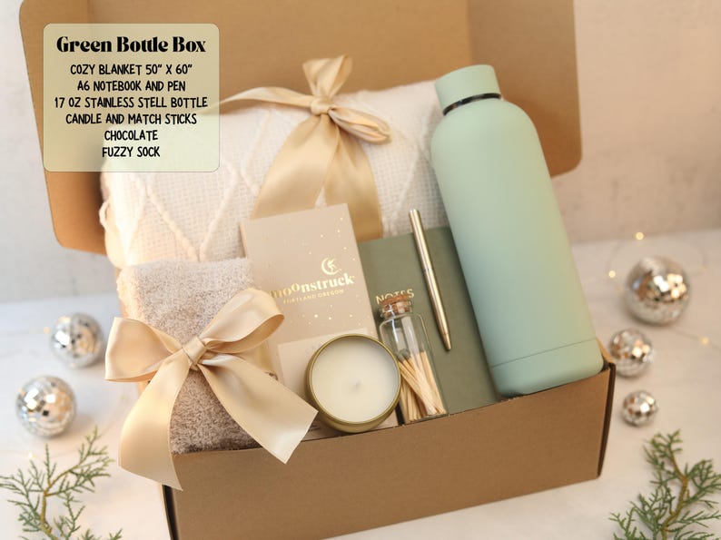 May include: A gift box containing a 50" x 60" white knit blanket with a gold ribbon, a 17 oz stainless steel bottle, a notebook, a pen, a candle, match sticks, chocolate, and a fuzzy sock. Text on the box reads: Green Bottle Box, Cozy Blanket 50" x 60", A6 Notebook and Pen, 17 oz Stainless Stell Bottle, Candle and Match Sticks, Chocolate, Fuzzy Sock.
