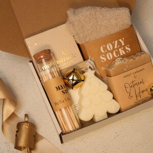 Puede incluir: Una caja de regalo que contiene un par de calcetines beige suaves, un frasco de vidrio con cerillas y tap&oacute;n de corcho, un cascabel dorado, una vela blanca con forma de &aacute;rbol de Navidad y una pastilla de jab&oacute;n de caramelo, avena y miel.