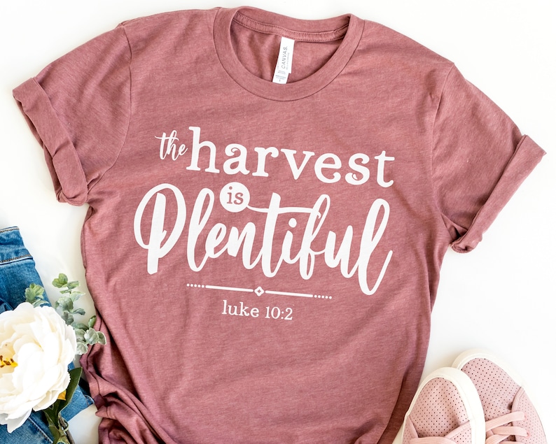 K&ouml;nnte beinhalten: Ein mauvefarbenes T-Shirt mit dem Text "the harvest is plentiful" und "luke 10:2" in wei&szlig;er Schrift.