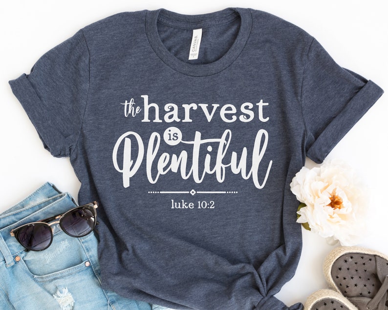 K&ouml;nnte beinhalten: Ein marineblaues T-Shirt mit wei&szlig;em Text, der "the harvest is plentiful" und "Luke 10:2" lautet.