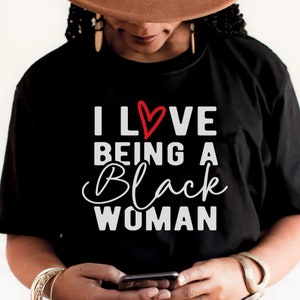 May include: Black t-shirt with the text "I LOVE BEING A BLACK WOMAN" in white lettering and a red heart.