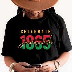 May include: A black t-shirt with the text "Celebrate 1865 Juneteenth" in red, green, and yellow lettering.