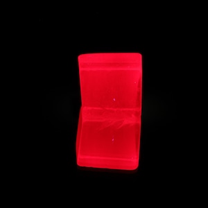 Könnte beinhalten: Eine leuchtend rote, offene Schmuckschatulle vor schwarzem Hintergrund. Die Schatulle ist rechteckig mit einem Klappdeckel und zeigt ein weiches Innenleben. Die leuchtende Farbe der Schatulle kontrastiert stark mit dem dunklen Hintergrund.