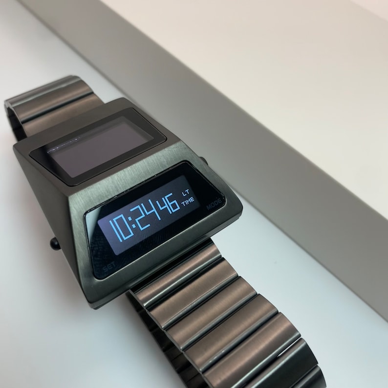 May include: A black digital watch with a silver face and a metal band. The watch face displays the time as 10:24:46. The watch has buttons labeled "SET" and "MODE".