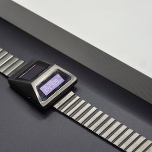 May include: A silver digital watch with a black face and a silver metal band. The watch face displays the time as 2:23:09 PM.
