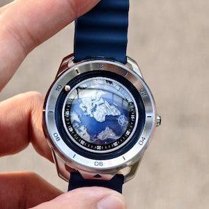 May include: A silver wristwatch with a blue band and a world map design on the face. The watch has a round face with numbers and markers around the edge. The band is a dark blue, ribbed silicone.