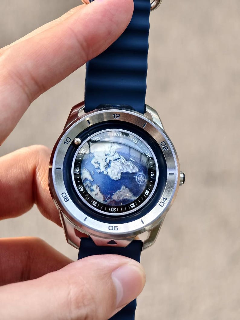 May include: A silver wristwatch with a blue band and a world map design on the face. The watch has a round face with numbers and markers around the edge. The band is a dark blue, ribbed silicone.