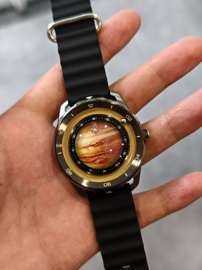 May include: A wristwatch with a black band and a round face featuring a detailed image of Jupiter. The watch has a silver-colored case and a black rubber strap. The watch face displays the time with white numerals.