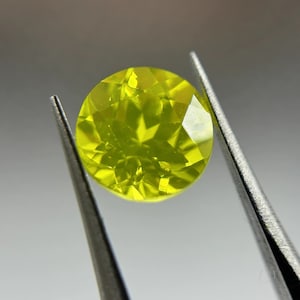 May include: A bright yellow gemstone with a faceted cut, held by tweezers.