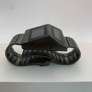 May include: A black digital watch with a metal band. The watch face is rectangular and has a digital display.