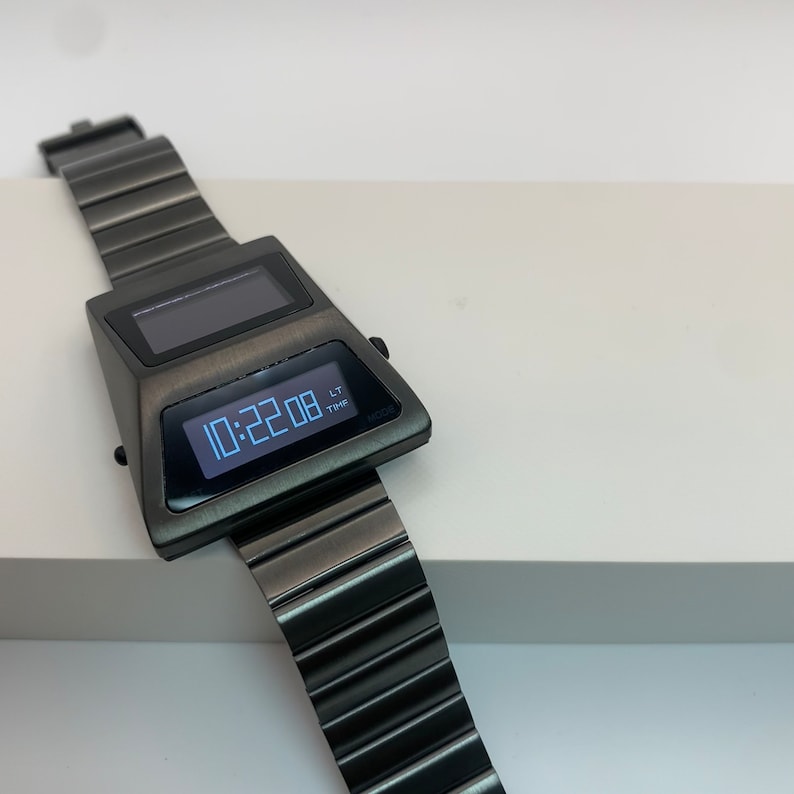 May include: A black digital wristwatch with a silver display showing the time 10:22:08. The watch has a black metal band and a rectangular face.