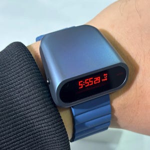 Könnte beinhalten: Eine blaue Digitaluhr mit rotem Display, das die Zeit 17:55:29 Uhr anzeigt. Die Uhr hat ein blaues Gummiband.