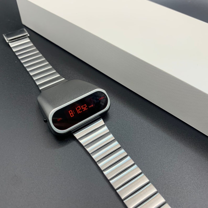 Op de afbeelding: Een zilveren digitale horloge met een rood LED-display dat de tijd 08:12:52 laat zien. Het horloge heeft een zilveren metalen band.
