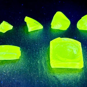 Könnte beinhalten: Sechs Stücke leuchtend gelbgrüner Fluoritkristalle auf einer dunkelblauen Oberfläche. Die Kristalle sind in verschiedenen Formen und Größen.