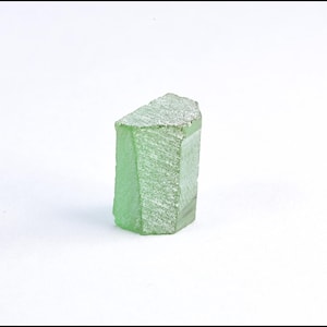 May include: A light green, rectangular crystal with a textured surface. The crystal has a faceted shape with a flat top and is set against a white background. The crystal is approximately 2 inches tall.