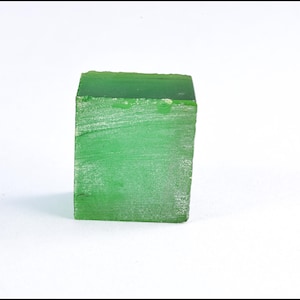 May include: A solid, rectangular block of green material. The block has a rough, textured surface with visible imperfections. The color is a vibrant, saturated green, and the block is set against a plain white background.