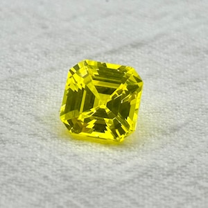 May include: A bright yellow gemstone with a square shape and a faceted cut.
