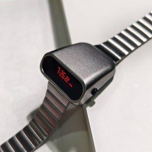 Op de afbeelding: Een zilveren digitale horloge met een rood LED-display dat de tijd 7:26:22 laat zien. Het horloge heeft een metalen band met een geribbeld ontwerp.
