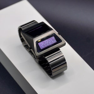 May include: A silver digital watch with a black face and a metal band. The time is displayed as 2:22:27 PM.