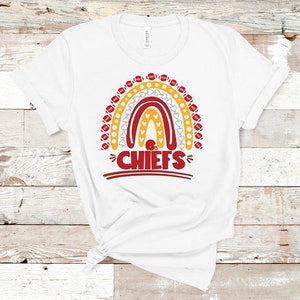May include: White t-shirt with a rainbow design made of footballs and hearts. The rainbow has the word "CHIEFS" in red letters at the bottom.