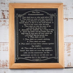 May include: A framed black slate plaque with the Ten Commandments engraved in silver lettering. The plaque has a wooden frame and is decorated with a decorative arch at the top. The text reads: "The Ten Commandments" and includes the text from Exodus 20.