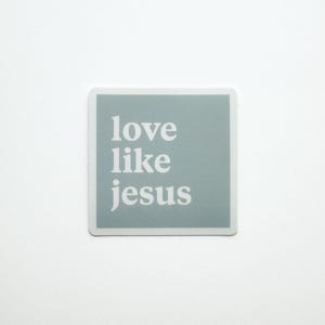 Puede incluir: Una pegatina cuadrada con las palabras "love like jesus" en blanco sobre un fondo verde azulado claro. La pegatina tiene un borde blanco y está sobre un fondo blanco.
