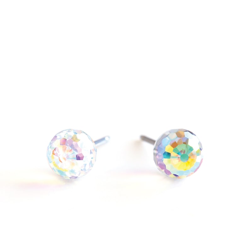May include: A pair of iridescent crystal ball stud earrings. Each earring features a faceted, spherical crystal with a silver post. The crystals reflect a rainbow of colors against a white background, creating a sparkling effect. Jewelry.