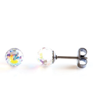 May include: A pair of stud earrings with iridescent, faceted crystal spheres. The earrings have a silver-tone post and backing. The crystal spheres reflect a rainbow of colors, creating a sparkling effect. The earrings are set against a white background.