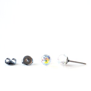 May include: A pair of clear crystal stud earrings with a faceted, spherical design. The earrings are shown with a post and backing, and are set against a white background. The earrings are approximately 0.3 inches in diameter.