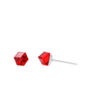 Könnte beinhalten: Ein Paar rote, facettierte Ohrstecker. Jeder Ohrring hat einen geometrischen, kubusförmigen roten Kristall auf einem silbernen Stecker. Die Ohrringe werden vor weißem Hintergrund präsentiert.