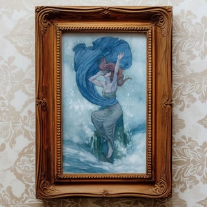 May include: A framed painting of a woman in a blue dress standing on a wave. The woman has red hair and is holding a blue cloth in her hand. The painting is set against a white background.