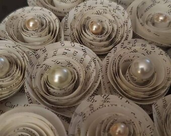 Peut inclure: Gros plan sur des fleurs en papier faites à la main avec des perles en leur centre. Les fleurs sont faites à partir de pages de livre, avec du texte visible. Les perles sont dorées, argentées et crème. Un objet décoratif unique.