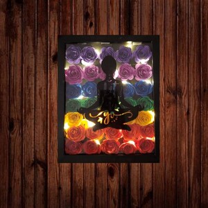 May include: A framed shadowbox art piece with a silhouette of a person in a yoga pose. The background is filled with colorful paper flowers in a rainbow pattern.