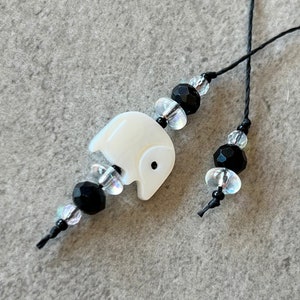May include: A white elephant charm with black eyes on a black string with clear and black beads.
